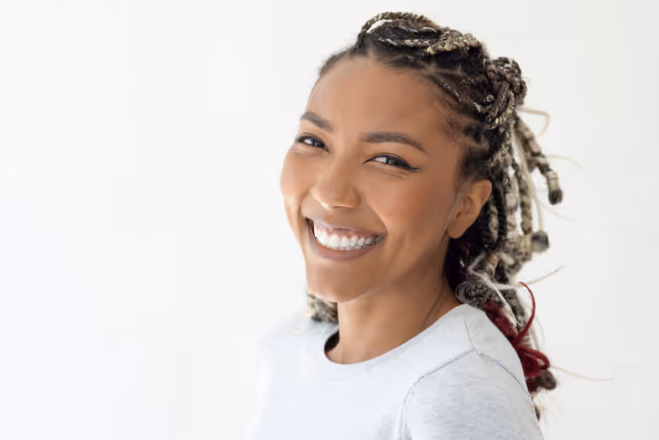 Smiling woman with braided hair wearing a white shirt against a plain light background.