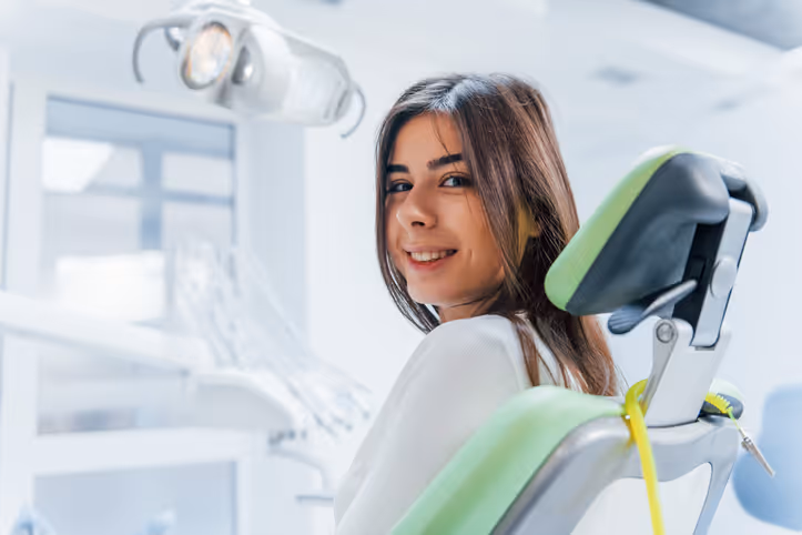 Young woman smiling while sitting in a green dental chair in a bright dental clinic.