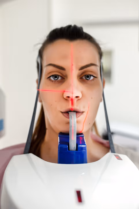 Close-up of a woman undergoing facial imaging with red laser lines marked on her face and a dental scanner in front of her mouth.