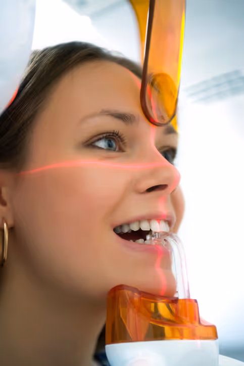 Young woman undergoing dental 3D scanning with red laser lines on her face and a dental scanner in her mouth.