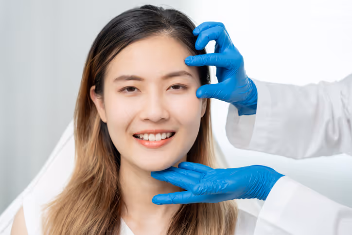 Smiling woman having her face examined by a professional wearing blue gloves.