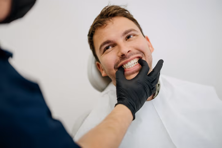 Male patient smiling as a dentist wearing black gloves examines his teeth in a dental office.