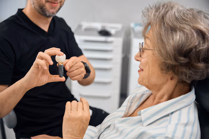 Dentist showing an elderly woman a dental implant model in a clinic.