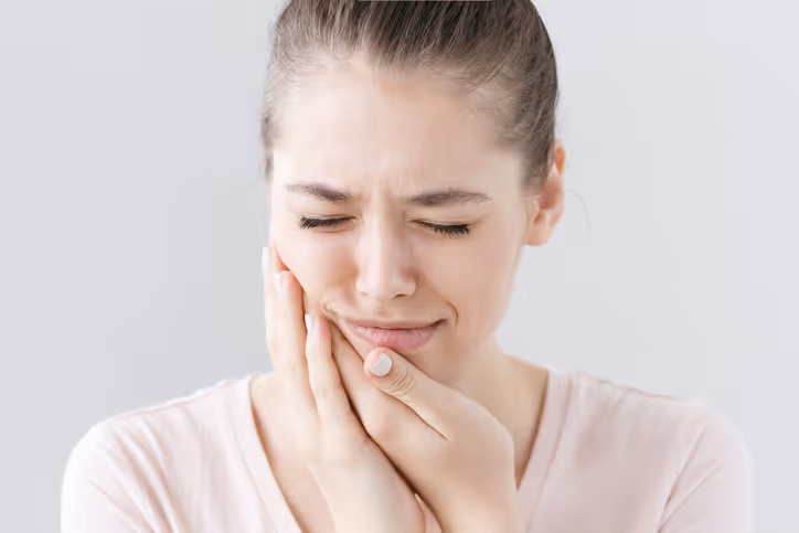 Young woman with eyes closed holding her cheek in pain, indicating a toothache.