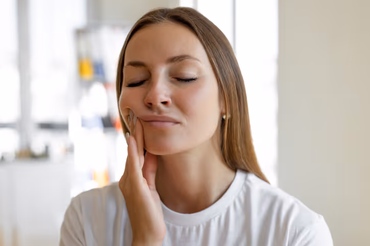 Young woman with eyes closed pressing her hand to the side of her face, showing discomfort or tooth pain.