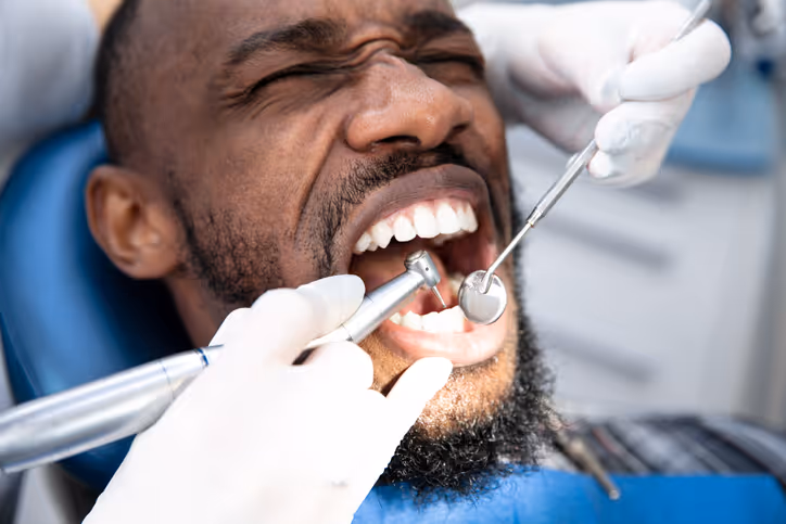 Man with eyes closed receiving dental treatment with dental drill and mirror inside mouth.
