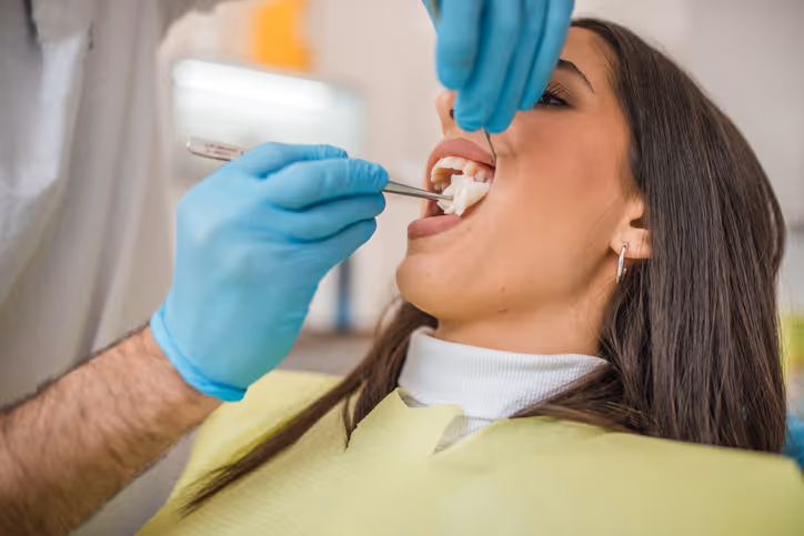 Dentist wearing blue gloves performing a dental procedure on a female patient reclining in a dental chair.