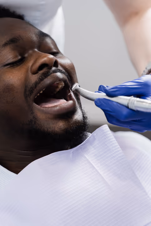 Dentist wearing blue gloves performing dental procedure on a man with mouth open in a dental chair.