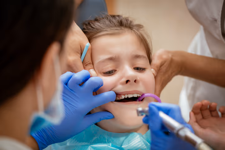 Young girl in dental chair receiving treatment with dental tools and gloved hands inside her mouth.