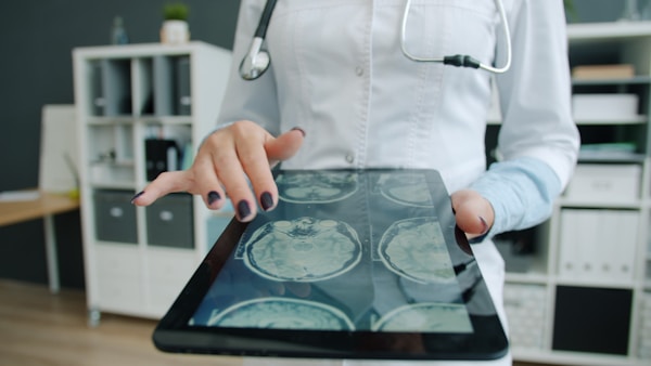 Close-up of woman's hand touching tablet screen with MRI images, doctor is working in office checking examination results. People and devices concept.