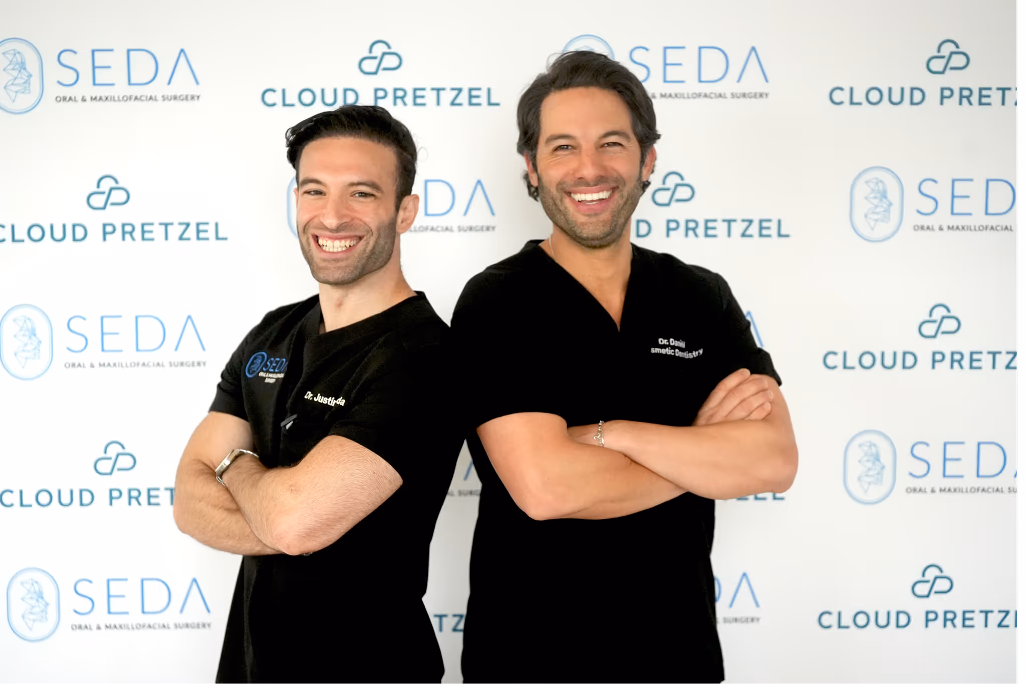 Two smiling men in black medical scrubs standing back to back with arms crossed in front of a backdrop with Seda Oral & Maxillofacial Surgery and Cloud Pretzel logos.