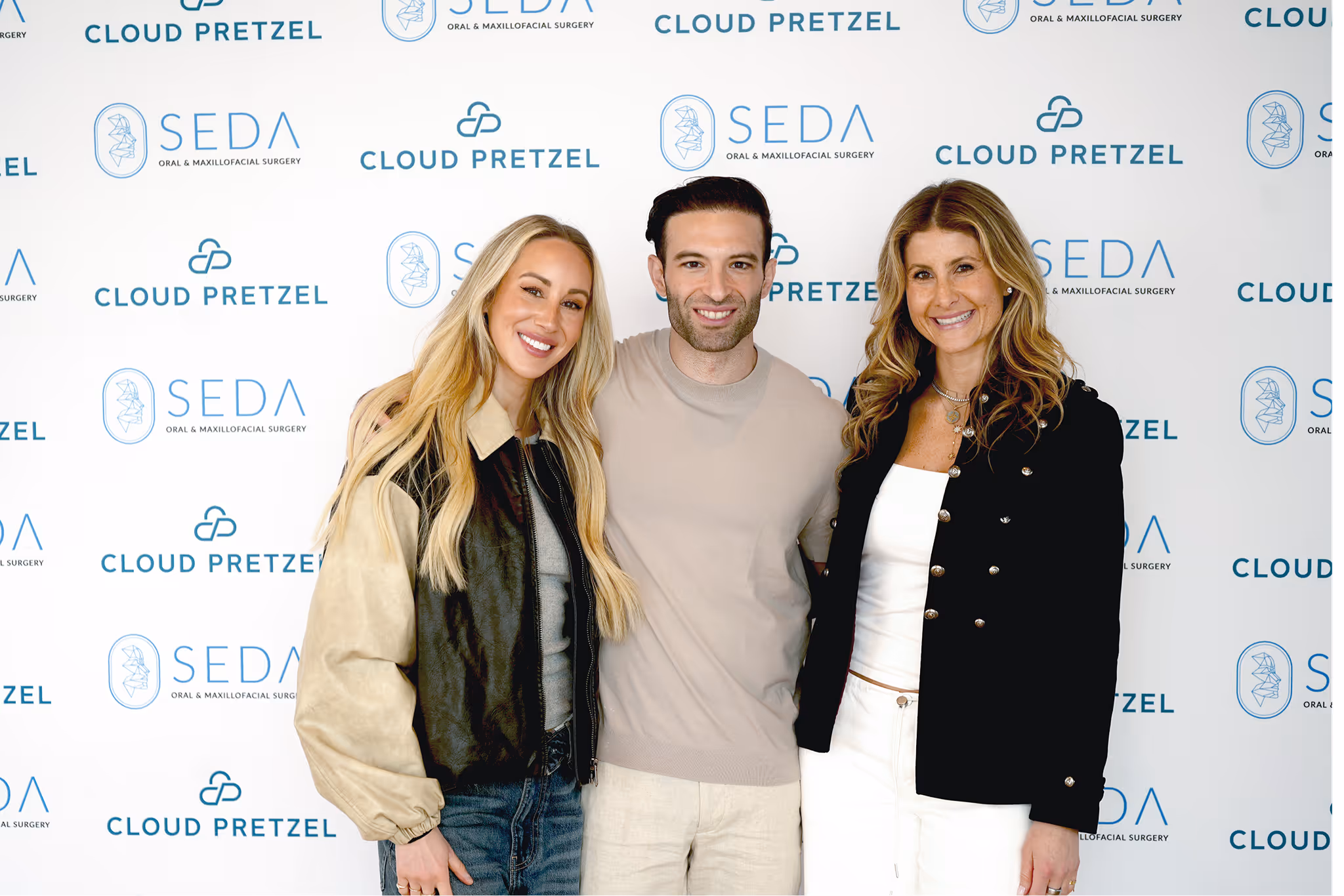 Three smiling people posing together in front of a backdrop with SEDA Oral & Maxillofacial Surgery and Cloud Pretzel logos.