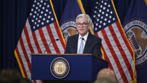 A person standing at a podium with flags behind himDescription automatically generated