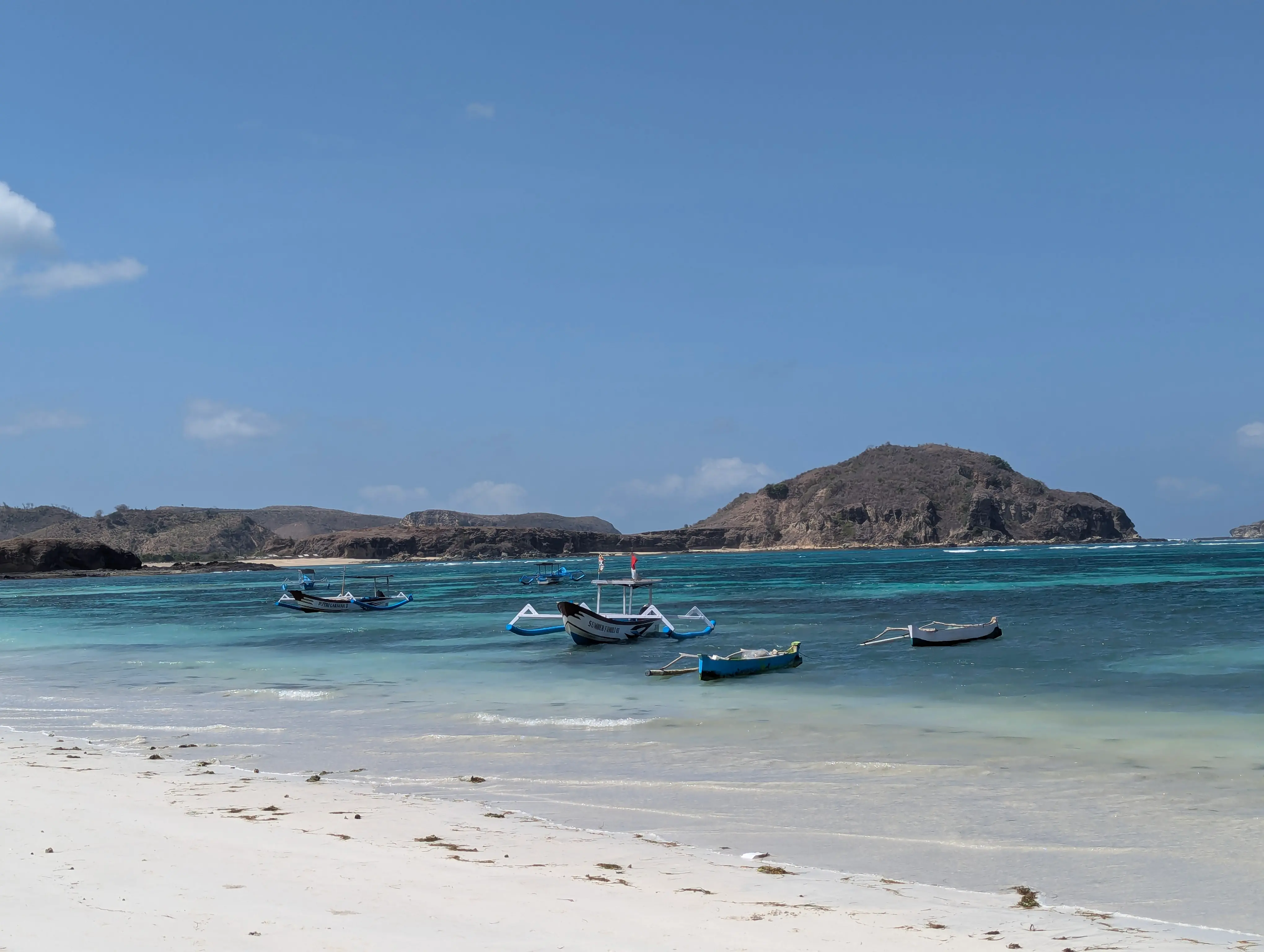 Outrigger fishing boats in turquoise water off the white sand of Tanjung Aan beach near Kuta, Lombok
