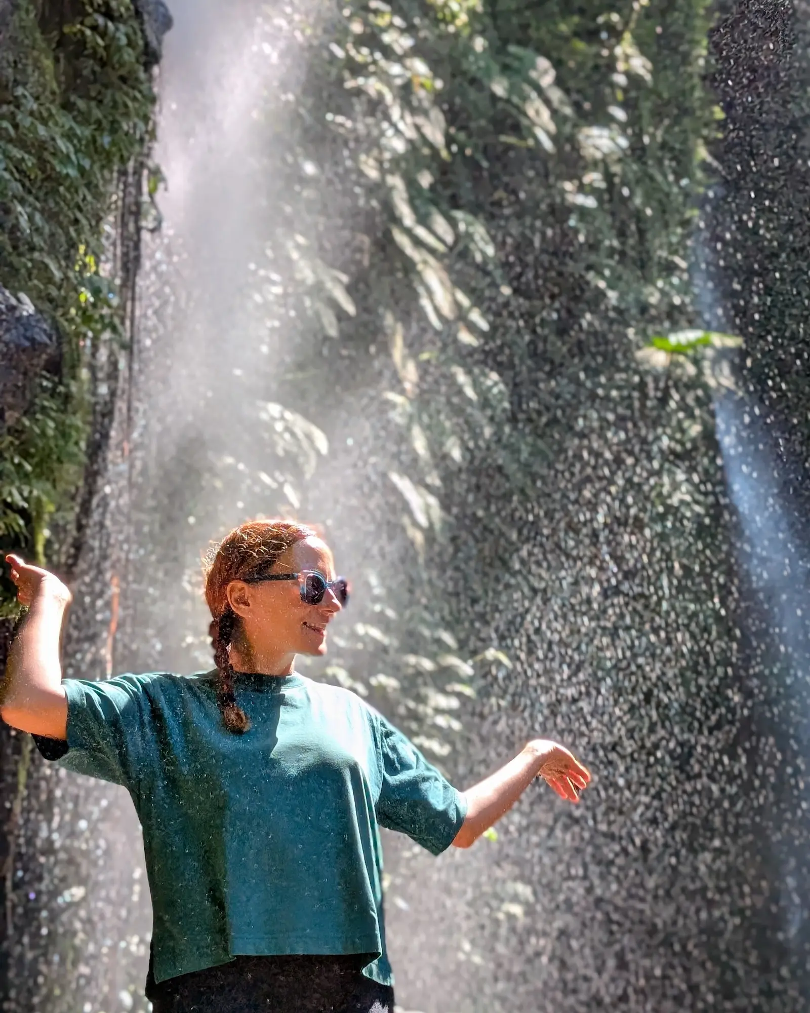 Sara Eloise Blangero smiling under the sunlit spray at Benang Kelambu waterfall in Lombok, Indonesia