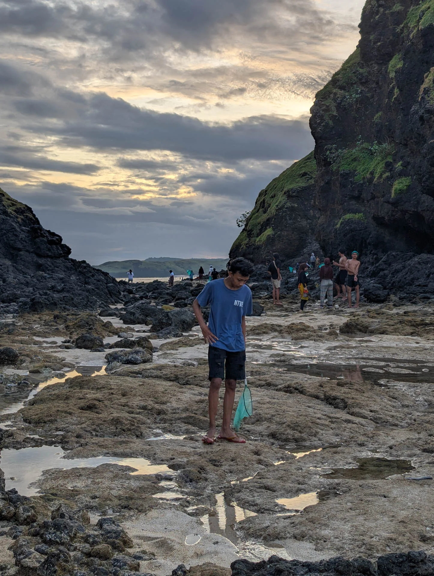 A boy holding a green net looks down into the rock pools below the cliffs at Seger beach