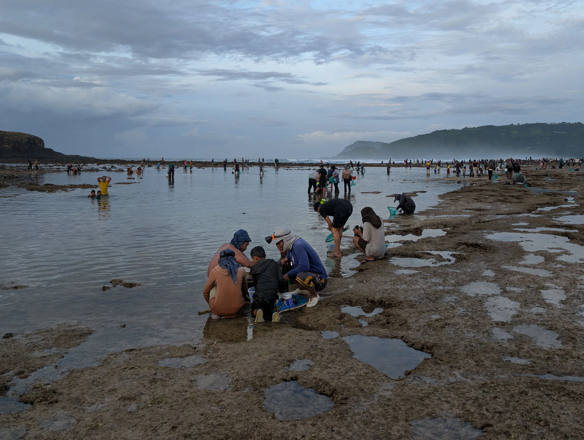 A family crouches over their net and buckets at the edge of a tide pool on Seger beach