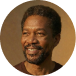 Portrait of a smiling middle-aged Black man with short hair and a goatee against a brown background.