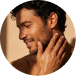 Smiling man with curly hair touching his neck, looking to the side with warm lighting.