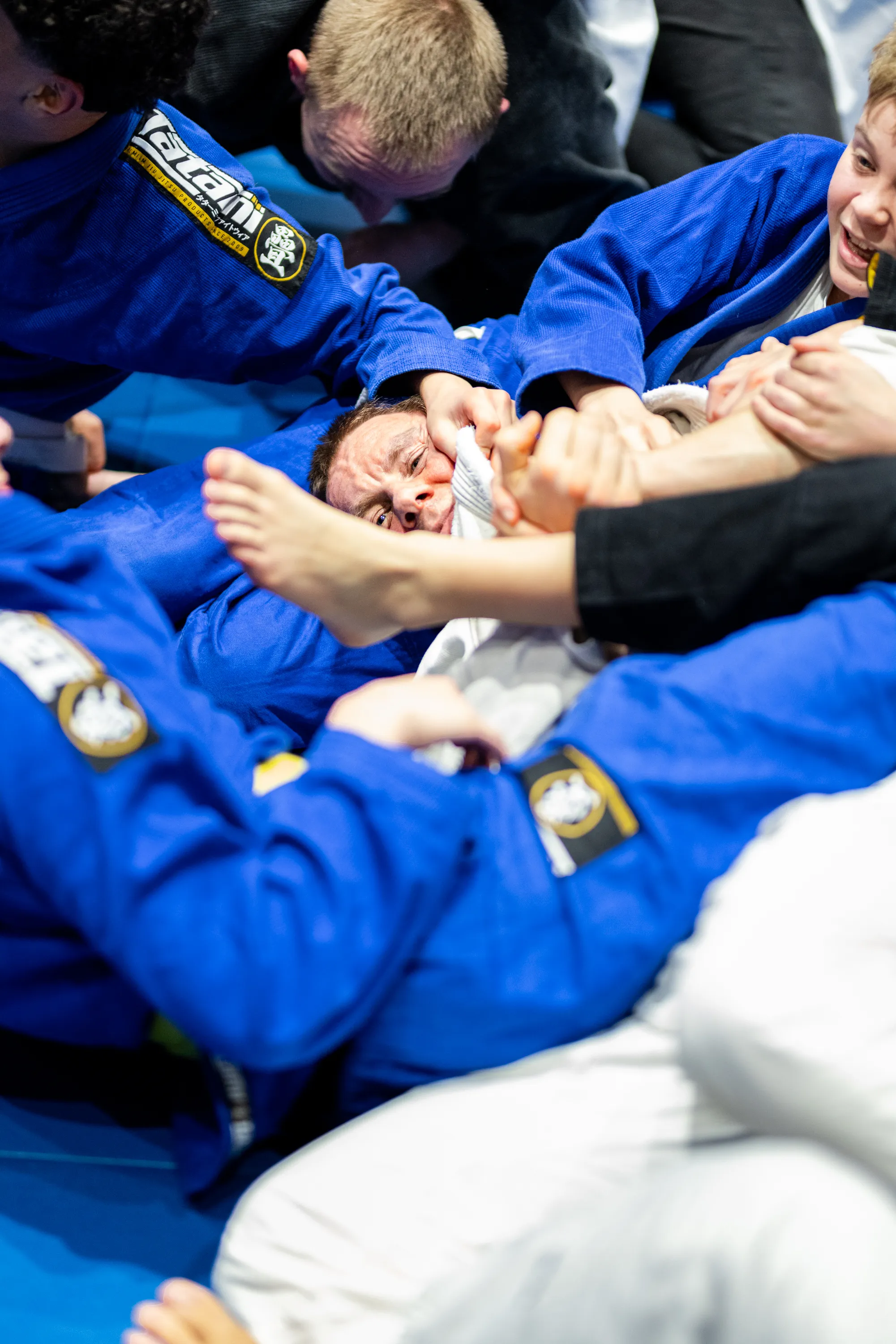 Group of people in blue Brazilian Jiu-Jitsu gis engaged in intense ground grappling.