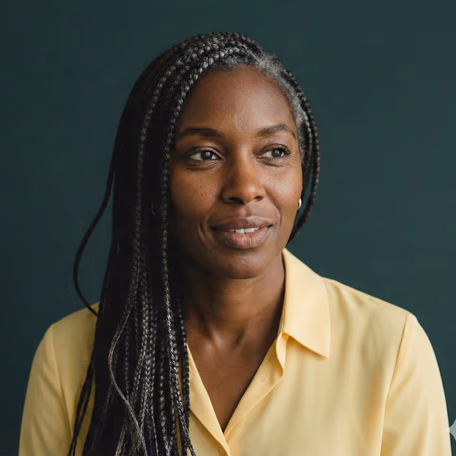 Portrait of a woman with long braided hair wearing a yellow shirt against a dark green background.