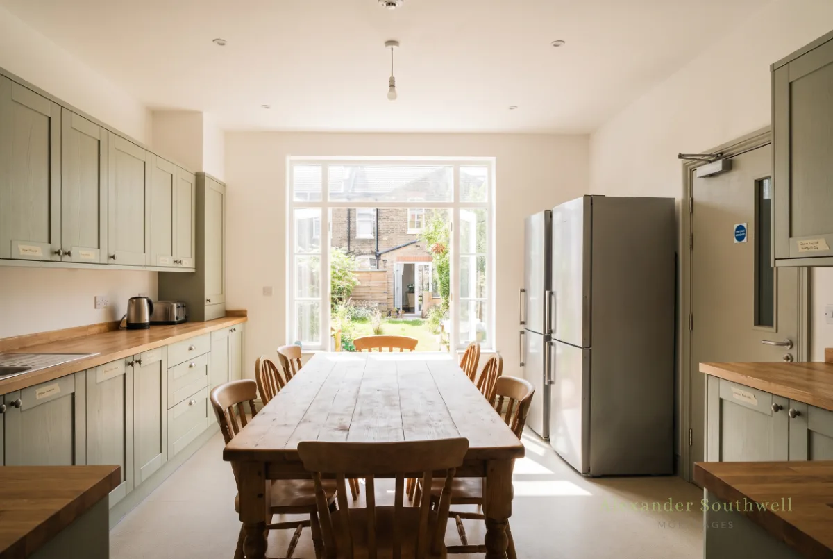 Shared kitchen in a UK HMO house share with a large dining table, two fridges and a fire door