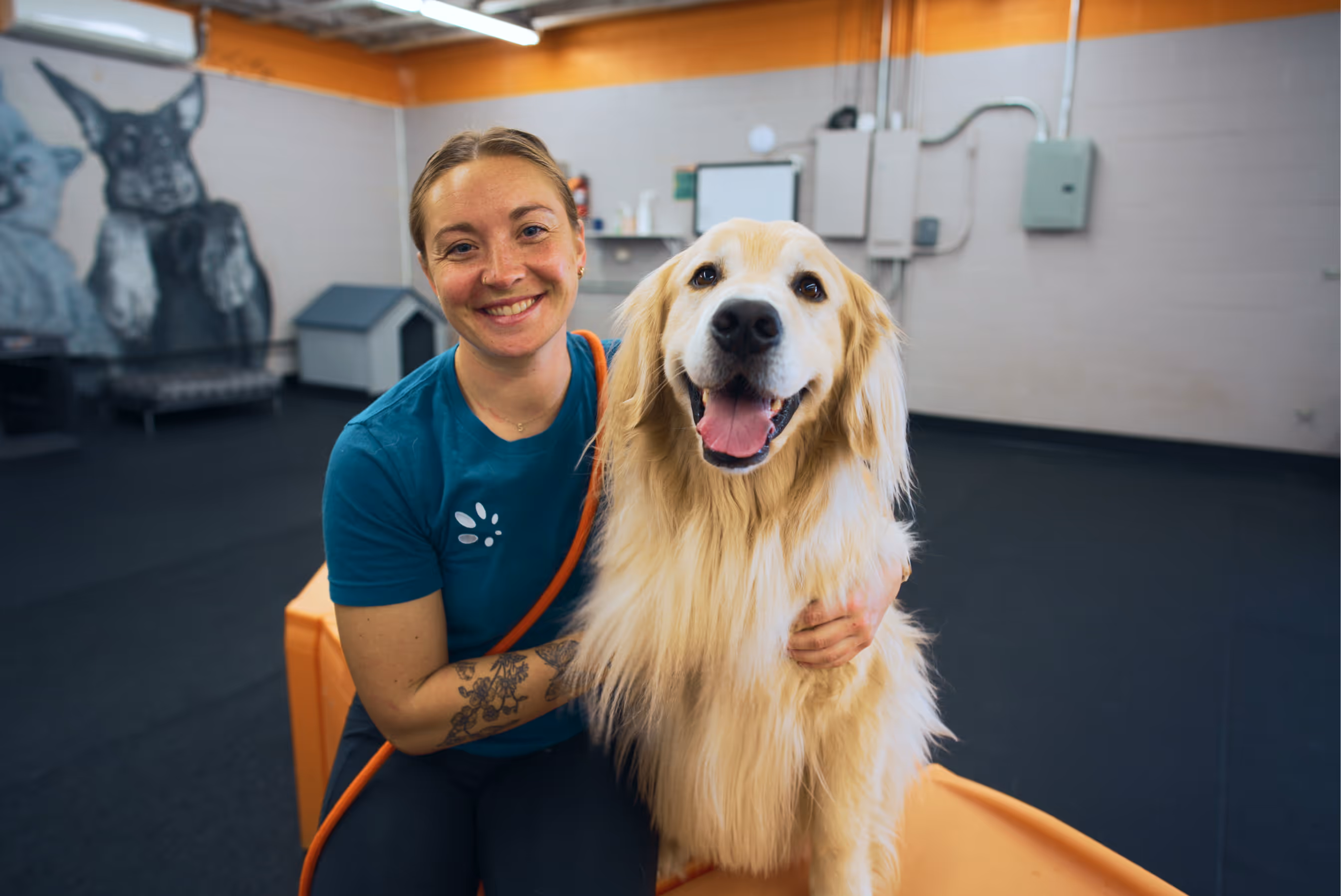 Smiling woman hugging a happy golden retriever dog inside a dog training or daycare facility.