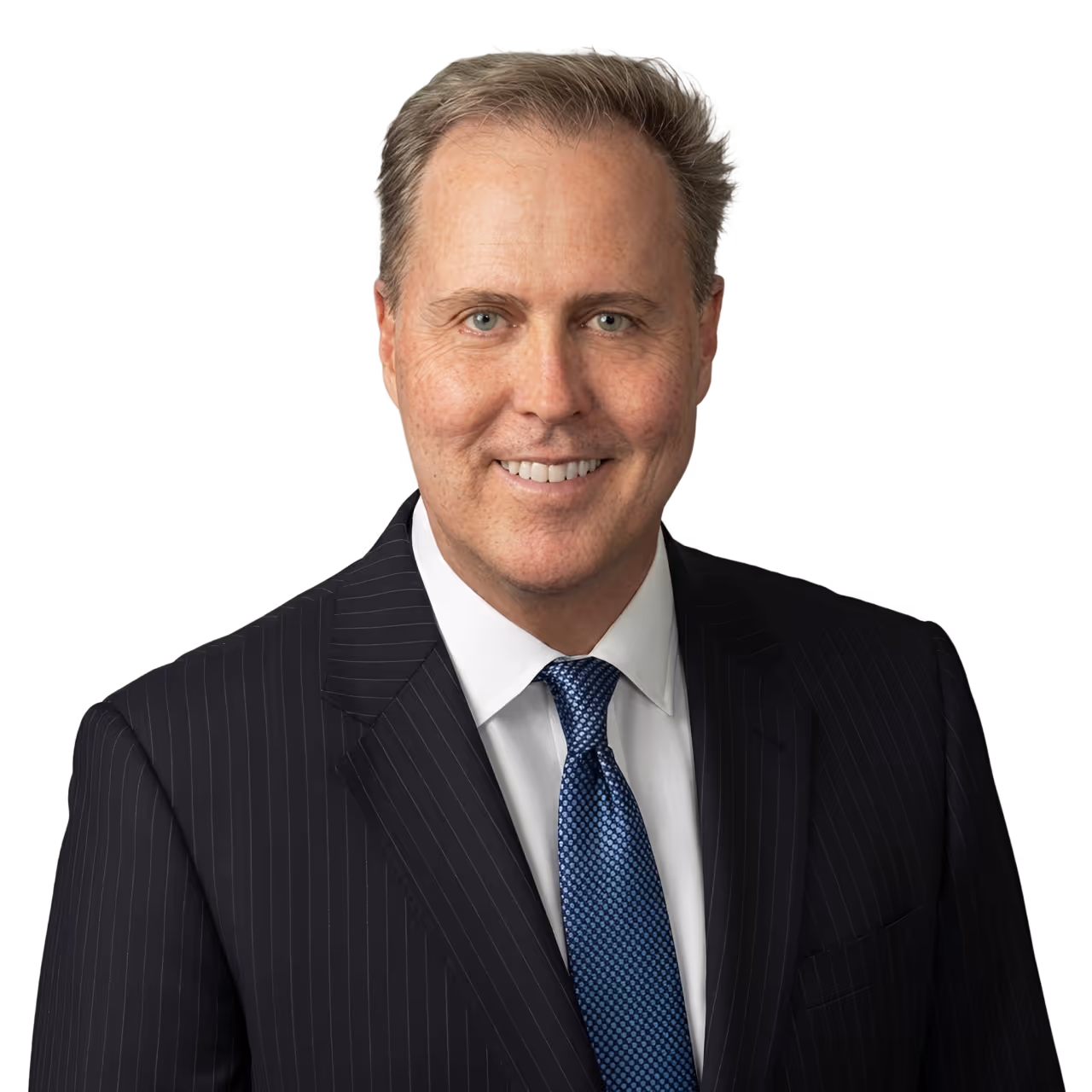 Smiling middle-aged man in a dark pinstripe suit, white shirt, and blue tie against a black background.