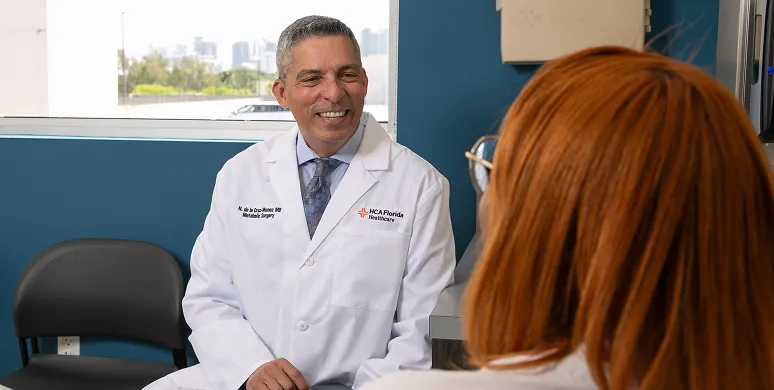 Dr. Nestor de la Cruz-Munoz in a white coat talking to a female patient with red hair in a medical office.