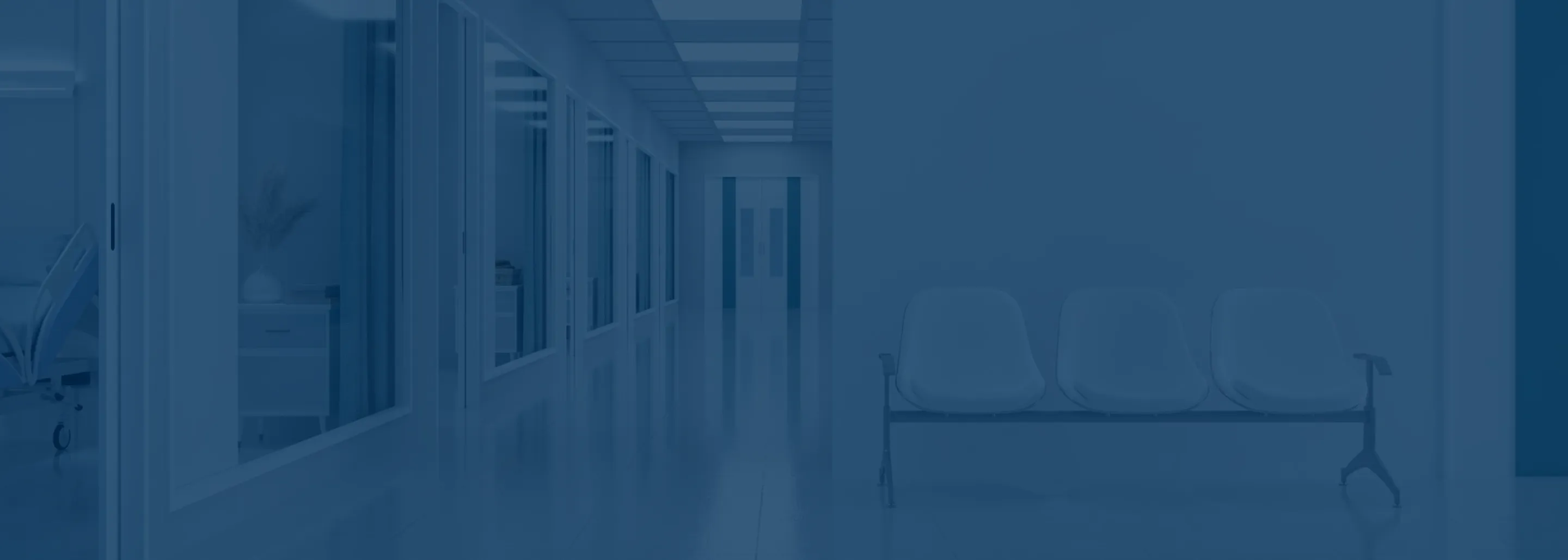 Empty hospital corridor with lined glass windows on the left and three connected waiting chairs on the right side.