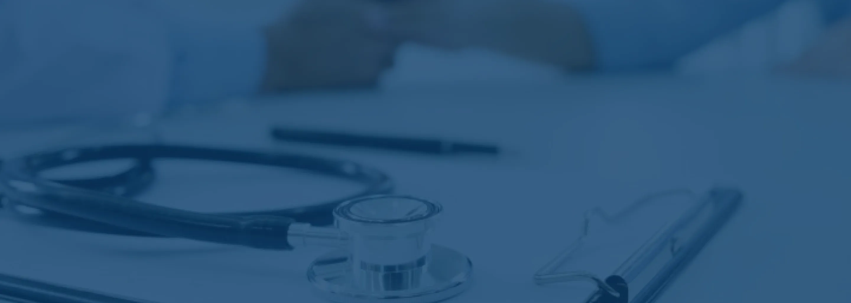 Close-up of a stethoscope, clipboard, and pen on a white surface, suggesting a medical or healthcare setting.