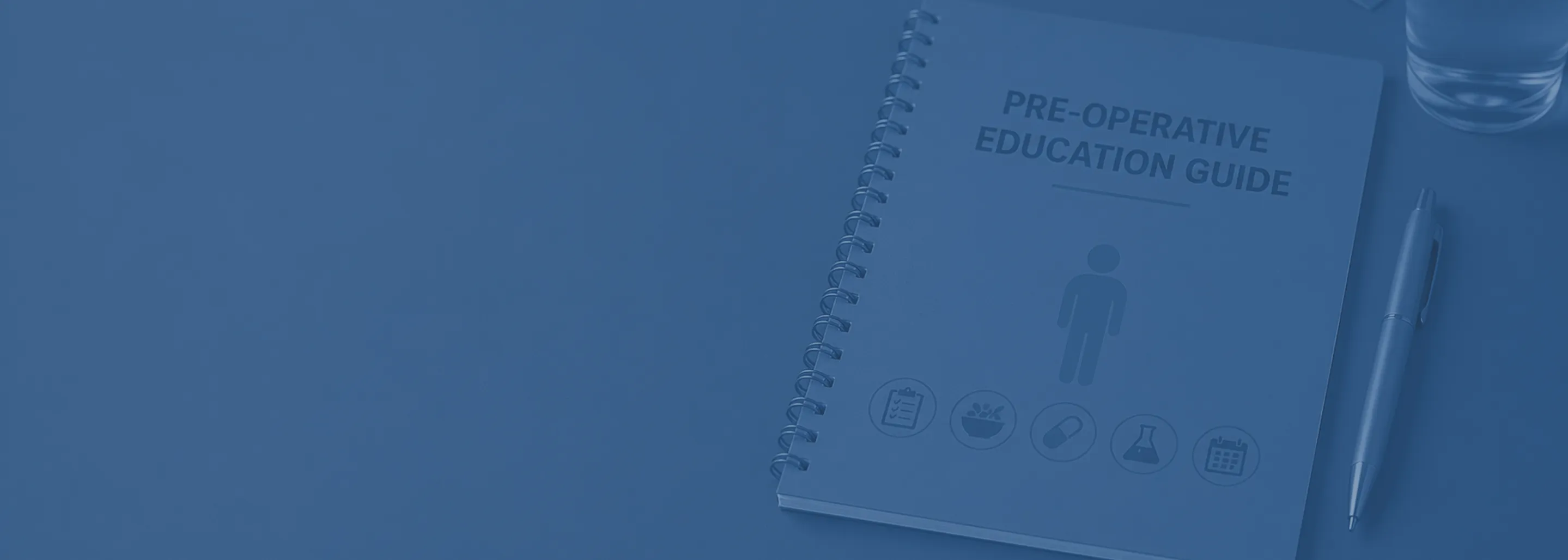 A spiral-bound booklet titled 'Pre-Operative Education Guide' with medical icons below the title, placed on a table next to a pen and a glass of water.