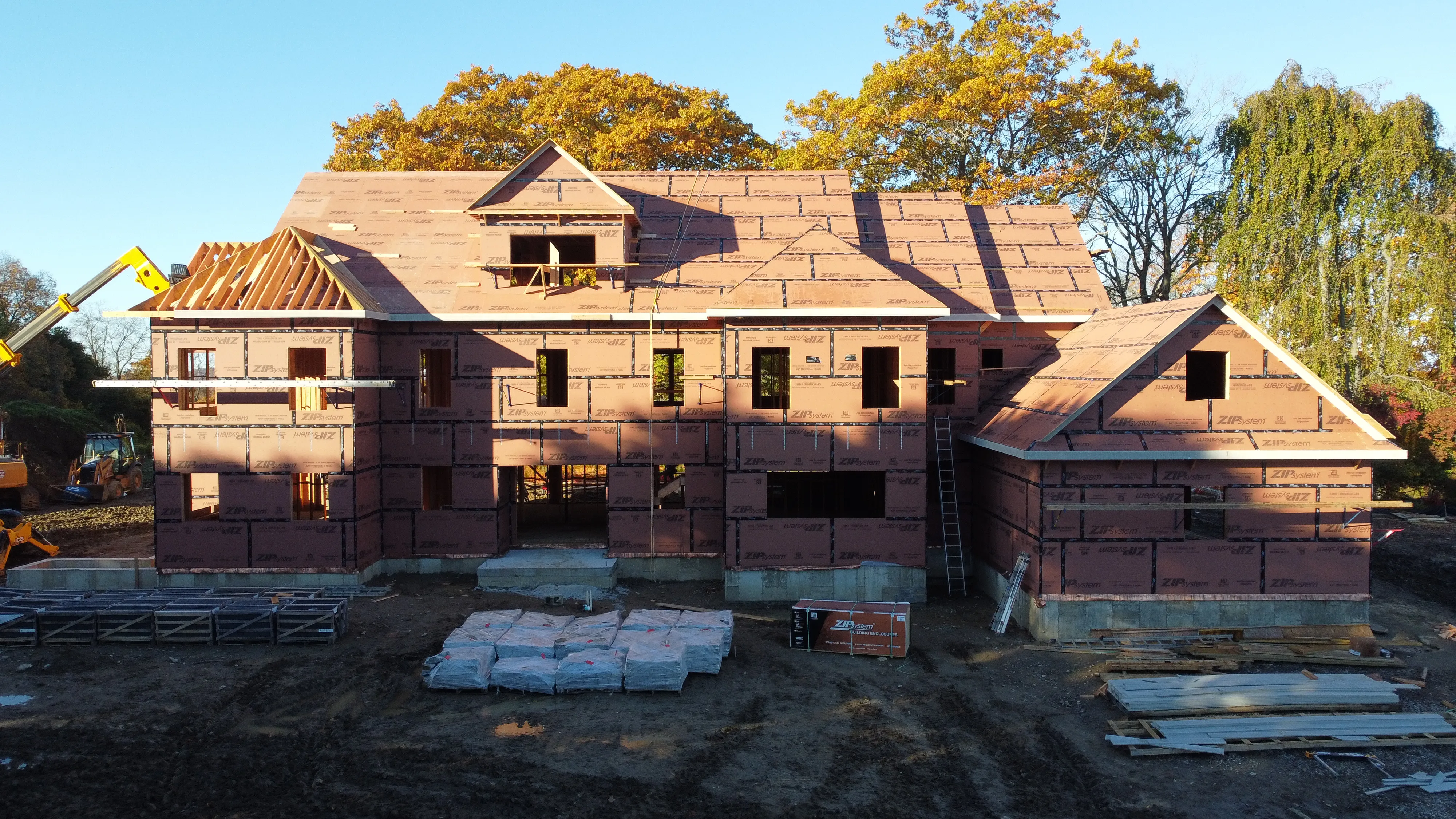 Partially constructed large residential house with exposed framing and sheathing under clear sky.
