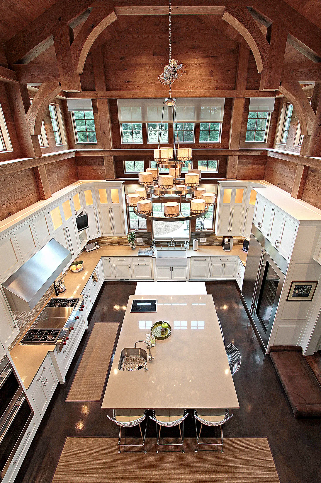Spacious modern kitchen with a large white island, stainless steel appliances, wooden ceiling beams, and a central chandelier.
