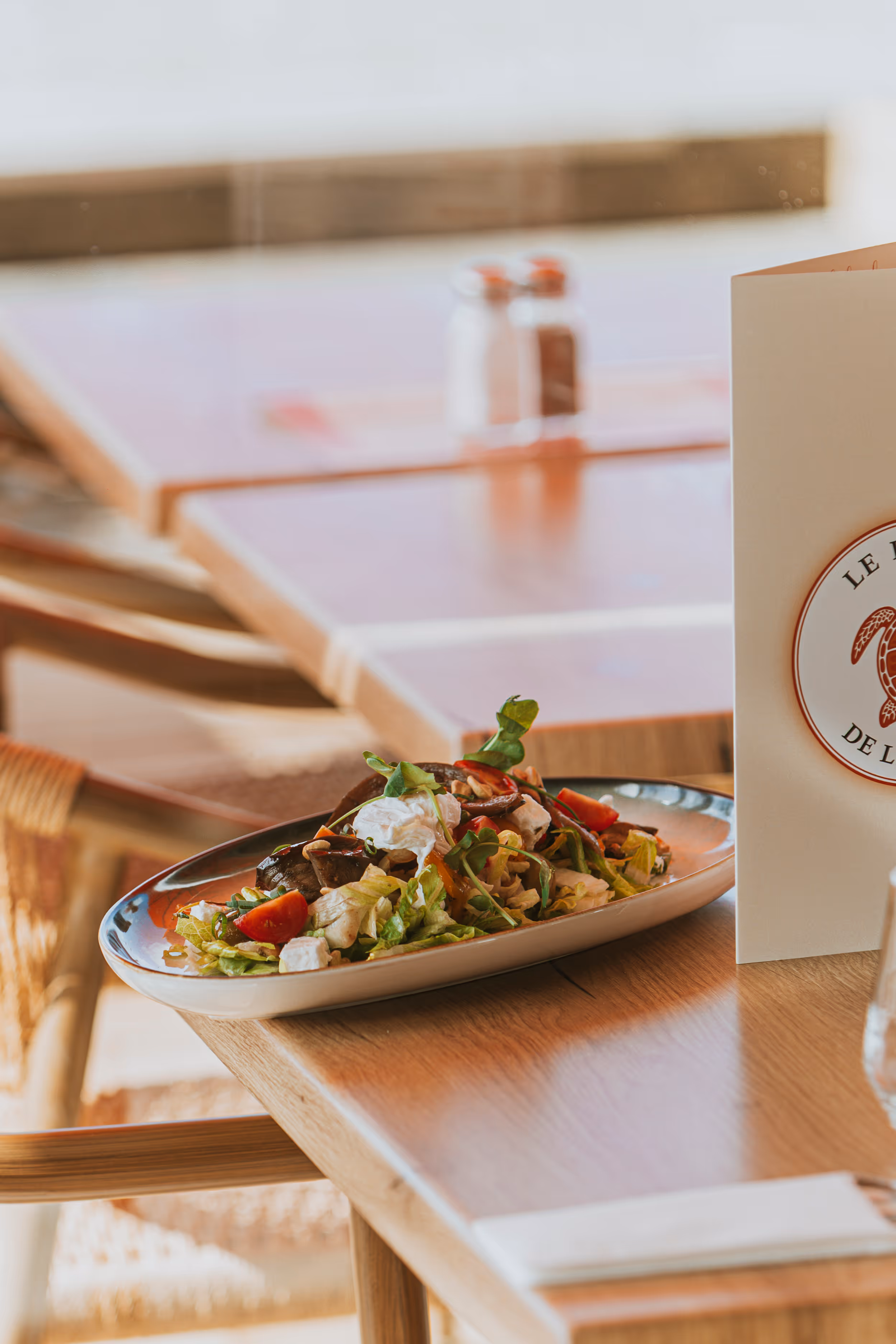 Salade fraîche avec tomates cerises, feuilles vertes et fromage sur une assiette ovale posée sur une table en bois dans un restaurant.