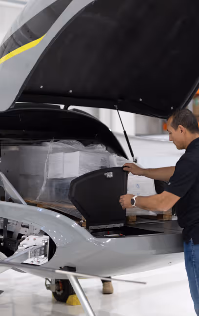 Man in black shirt opening a compartment on the front of a small aircraft inside a hangar.