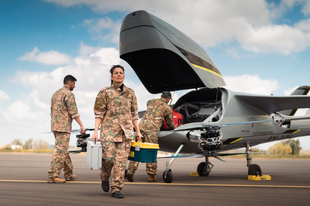 Military personnel working on an experimental aircraft with open rear compartment on a runway.