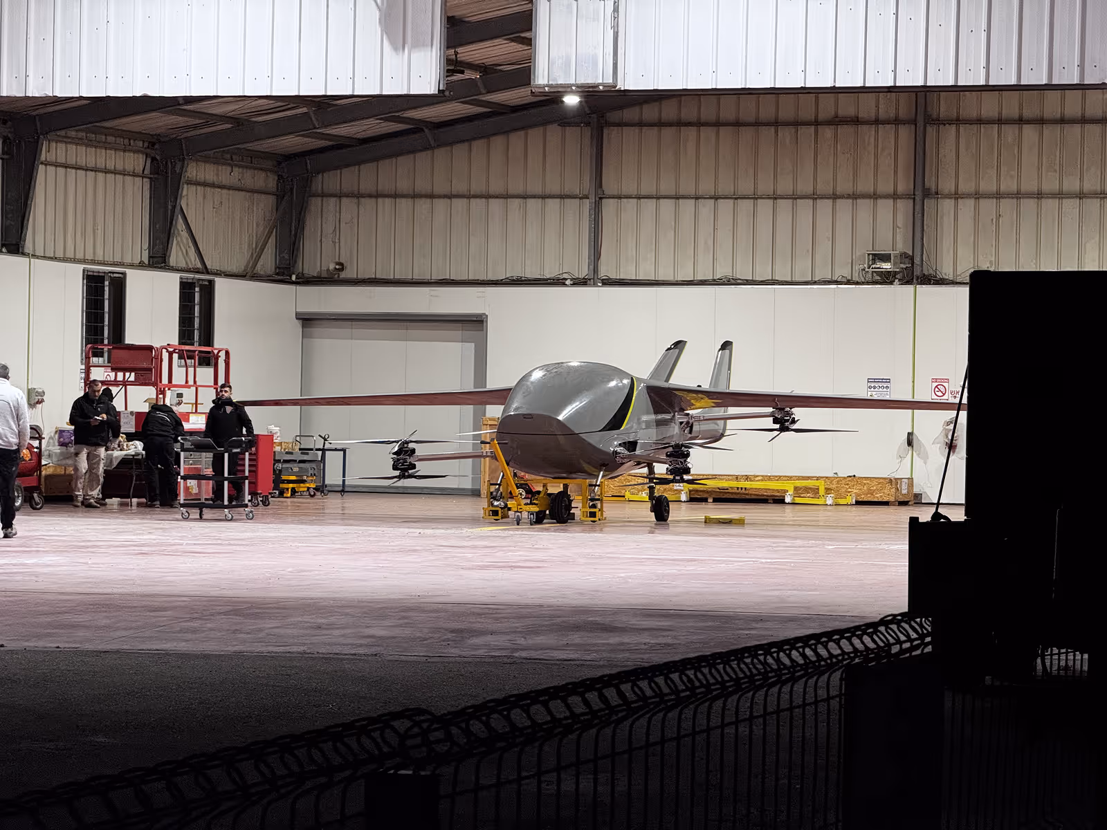 Large drone aircraft with multiple rotors inside a hangar with people and equipment nearby.