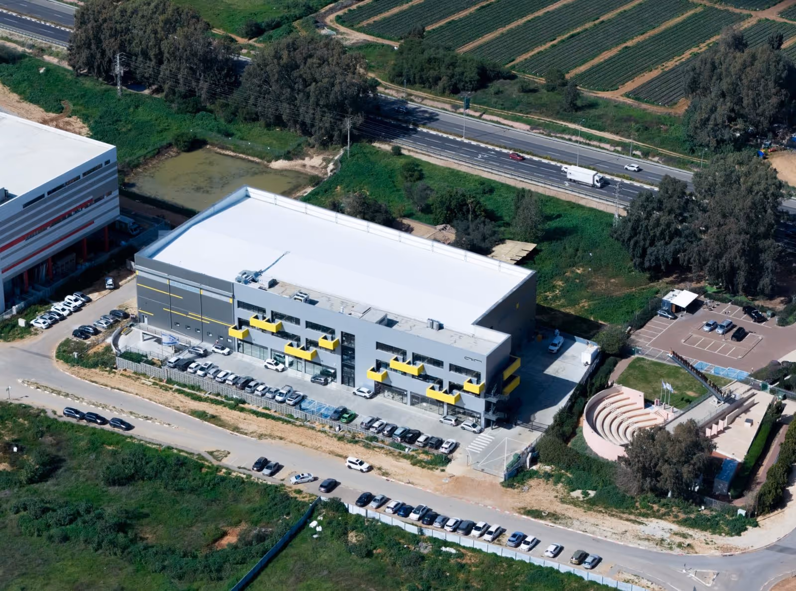 Aerial view of a modern gray building with yellow accents surrounded by parking lots and greenery.