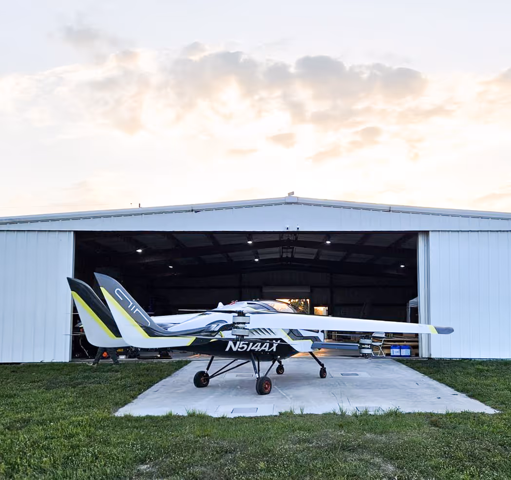 Small white and black aircraft with tail number N514AX parked outside a large hangar at sunset.