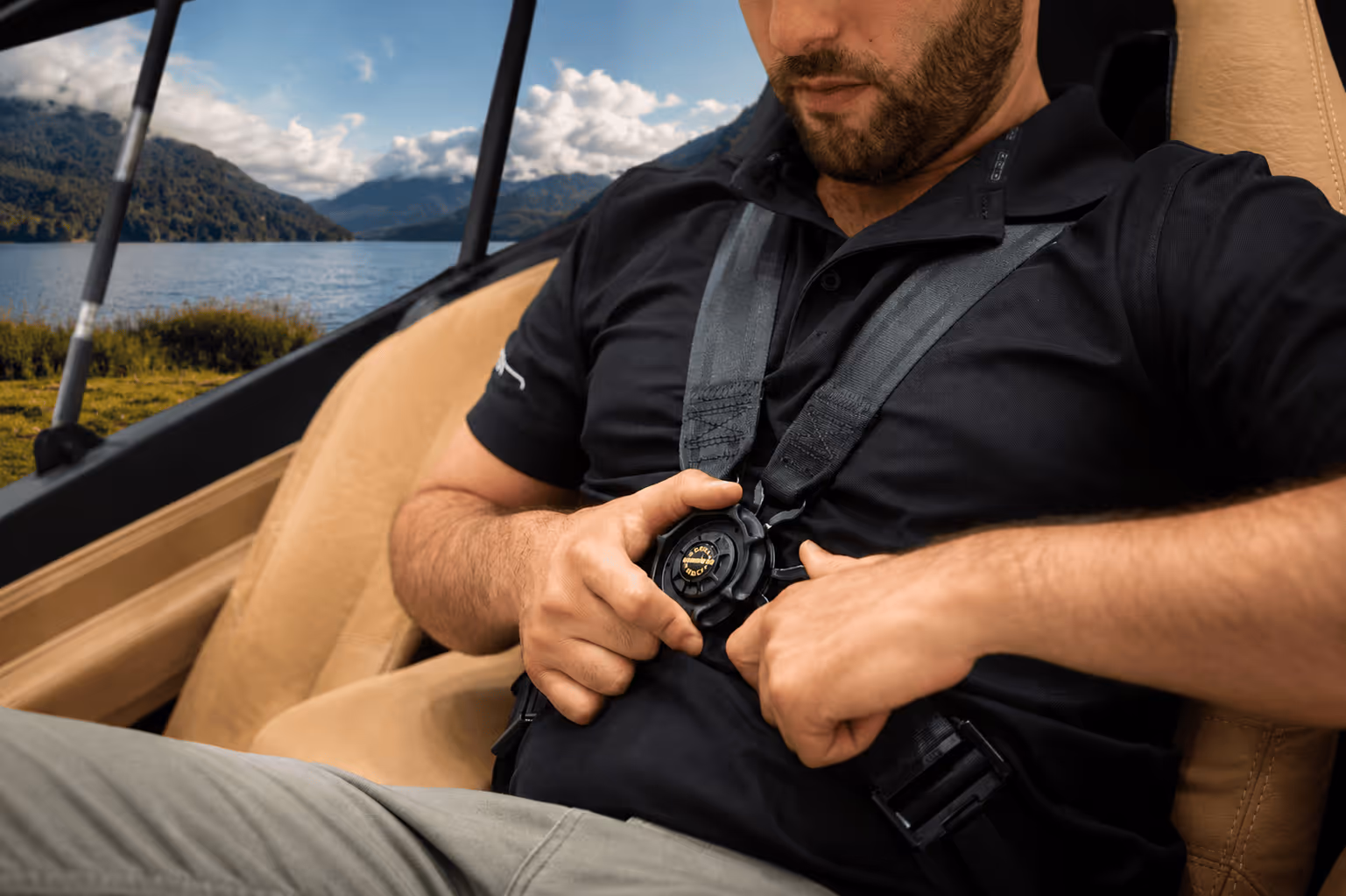 Man fastening a black safety harness while sitting in a beige car seat with mountains in the background.