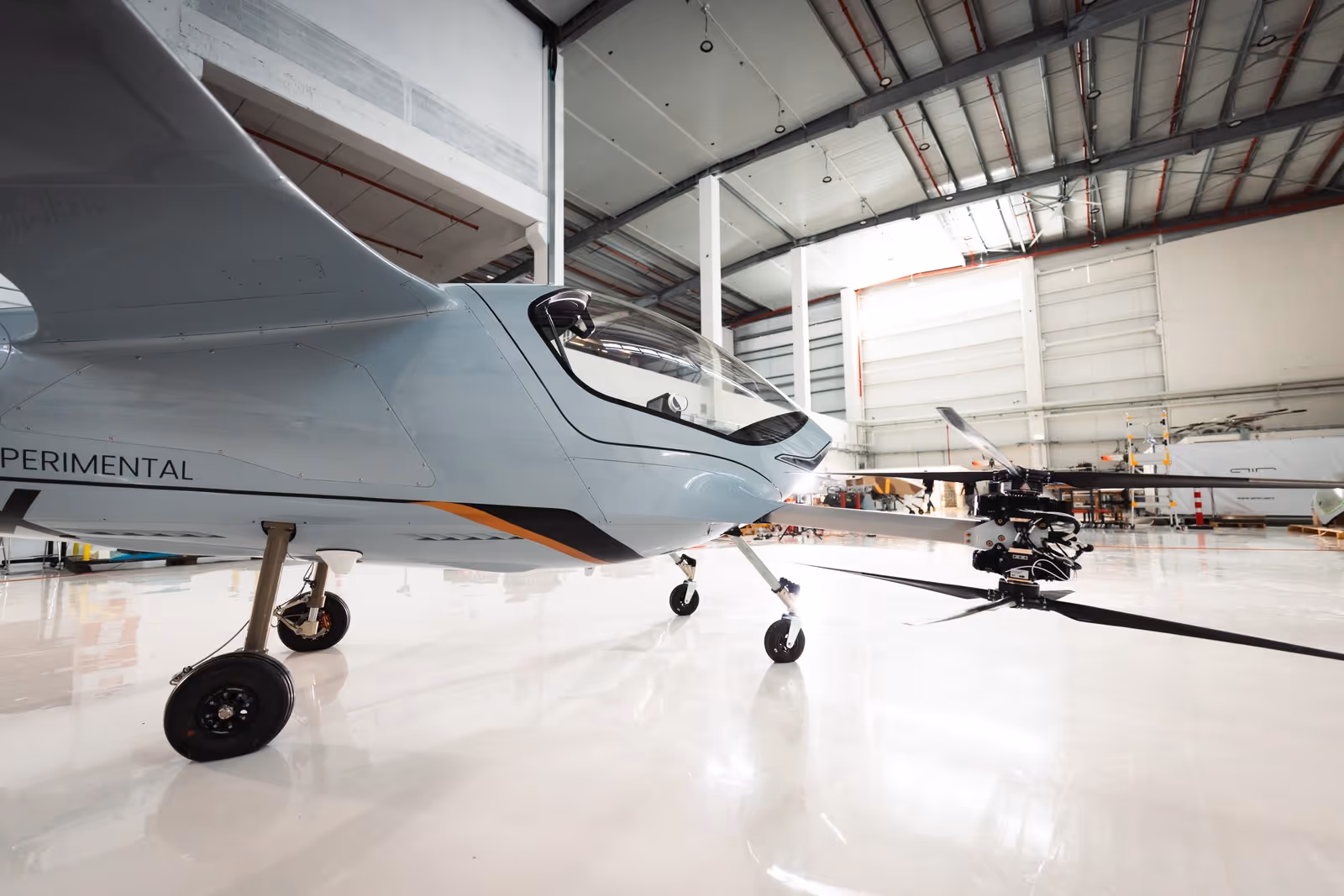 Close-up of an experimental light aircraft with three wheels inside a spacious hangar.