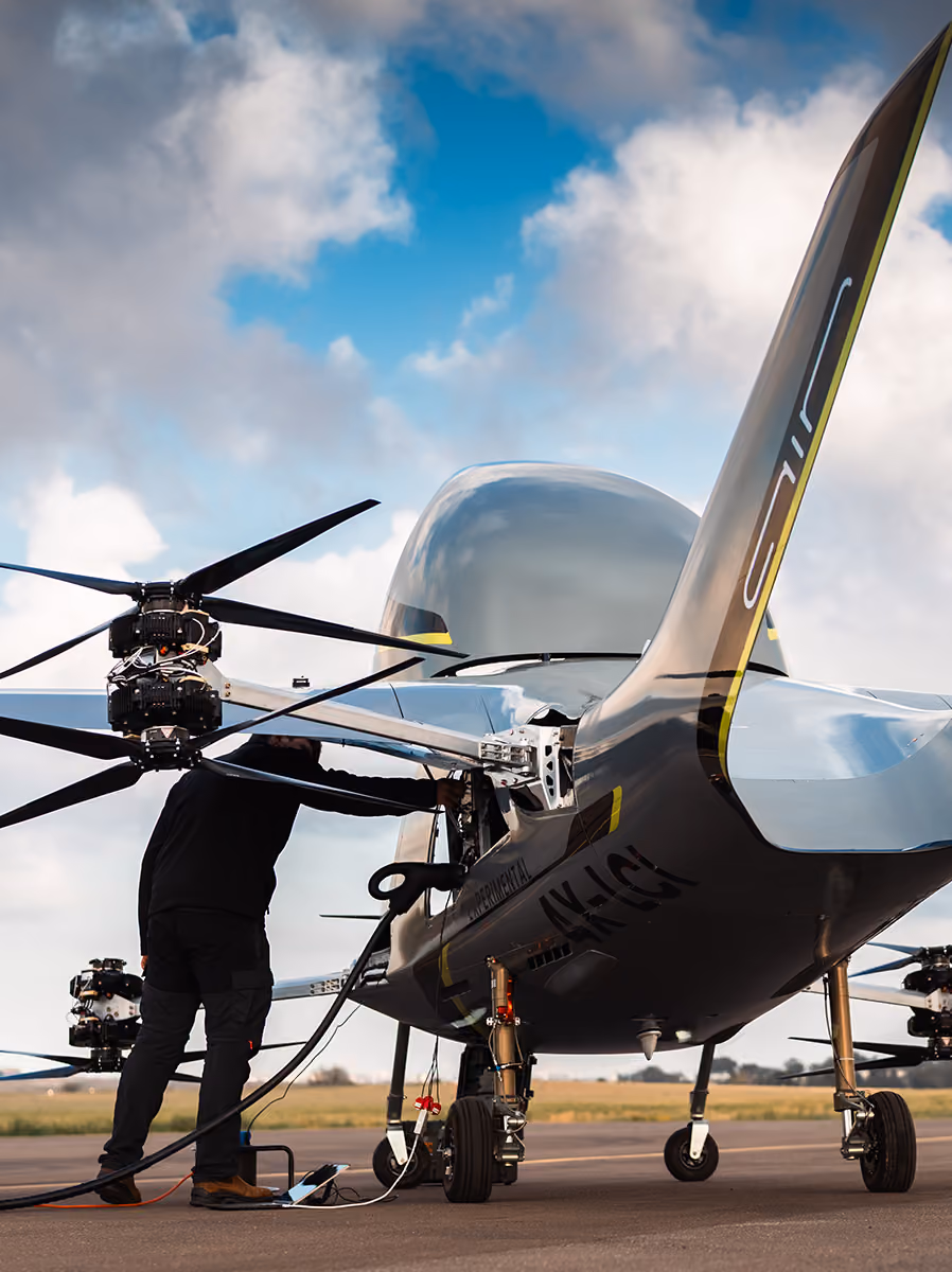 Person inspecting a drone aircraft on runway under partly cloudy sky.