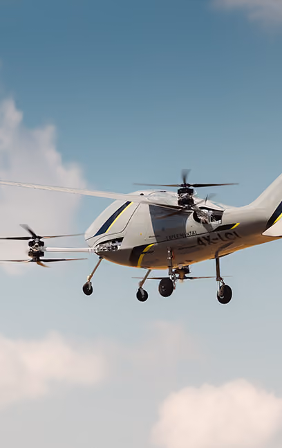 Modern white VTOL drone aircraft flying with spinning rotors against a blue sky with clouds.