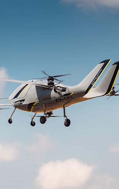 Futuristic white and yellow autonomous helicopter flying in a partly cloudy blue sky.