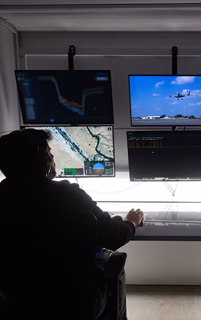 Person wearing headphones in front of four screens showing maps, charts, and an airplane in flight.