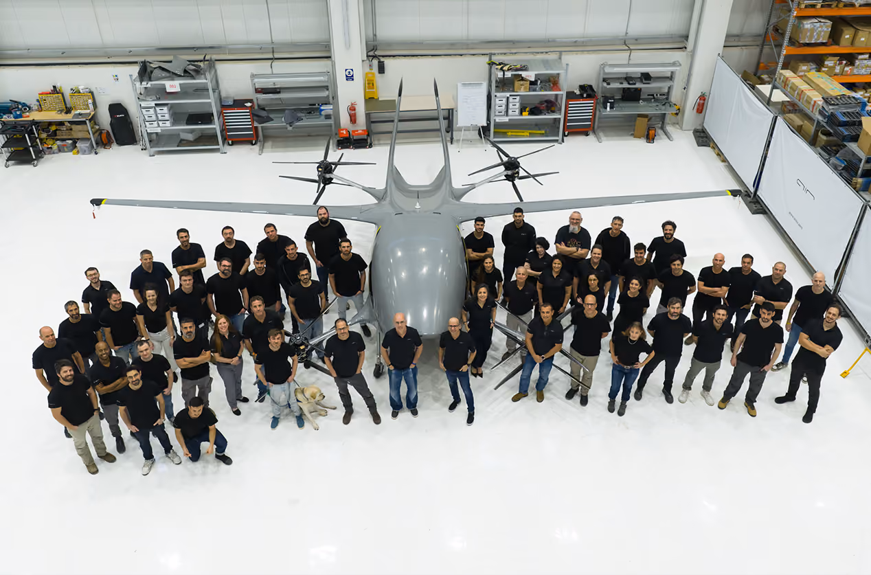 Group of people standing around a large drone in a spacious white industrial workshop.