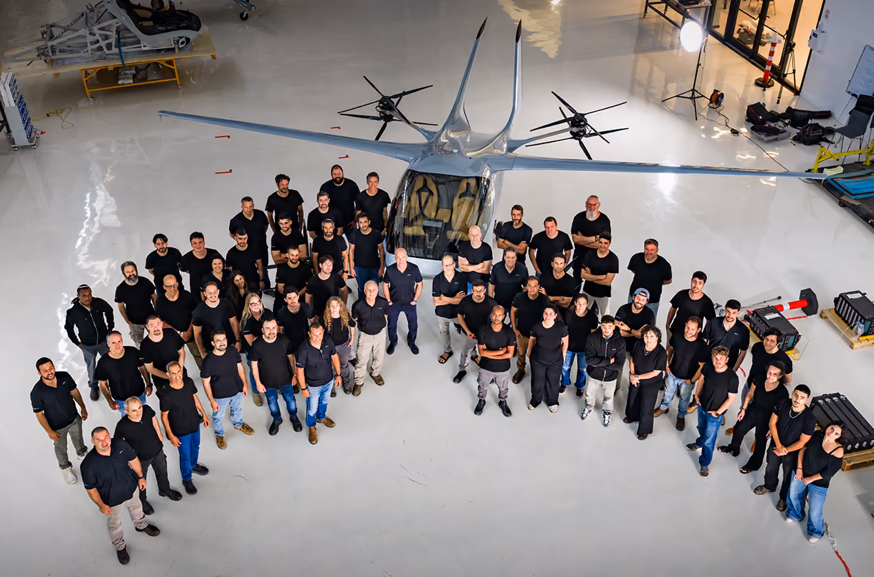 Group of people in black shirts standing around a futuristic drone aircraft in a spacious hangar.