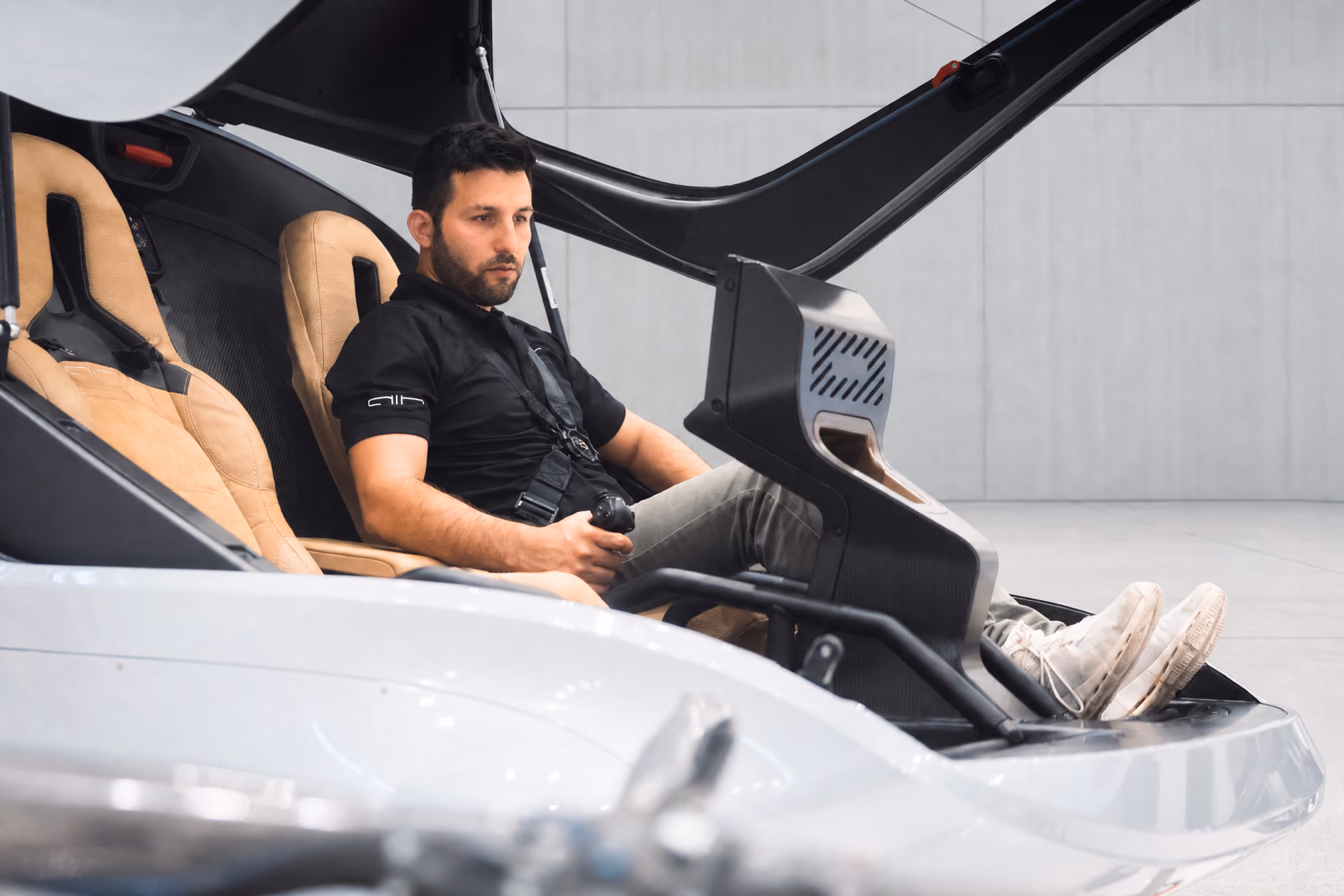 Man seated in a sleek cockpit simulator holding a joystick with feet resting on foot pedals.