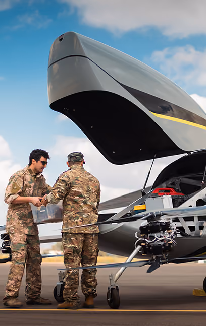 Two military personnel in camouflage uniforms handling equipment near an open drone on an airstrip.